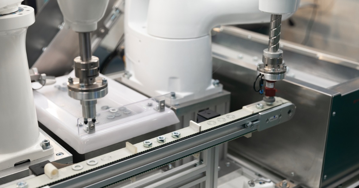 An automatic robot arm working in an industrial setting, inserting screws while another machine tightens them.