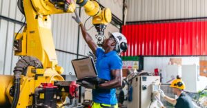 In an industrial warehouse, technicians are testing and troubleshooting a robotic fastening system with a robotic arm.