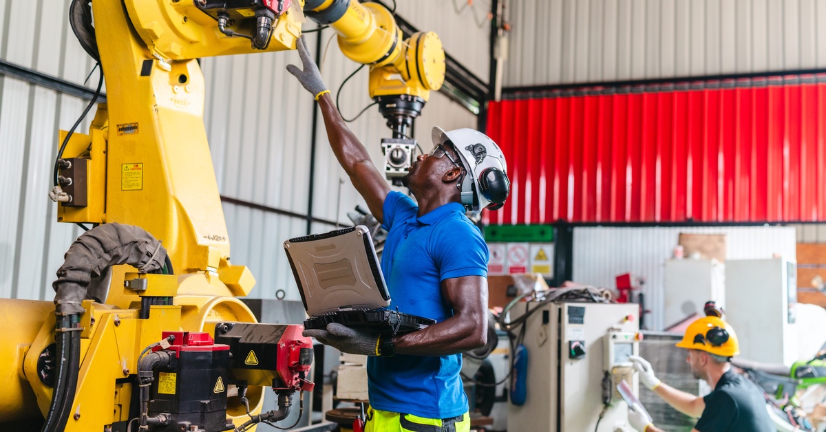 In an industrial warehouse, technicians are testing and troubleshooting a robotic fastening system with a robotic arm.