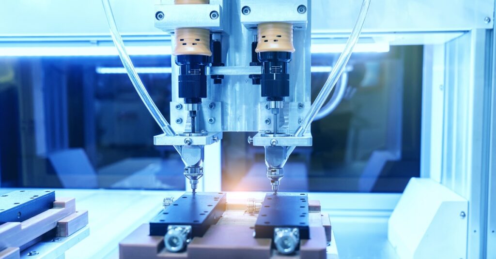 Two automatic screw feeder heads positioned over black fixtures inside a blue-lit electronics assembly machine.