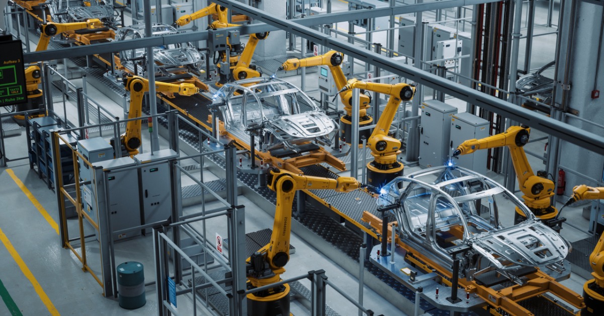 A car factory assembly line with robotic arms, unfinished vehicle frames, overhead lights, and green floor lanes.